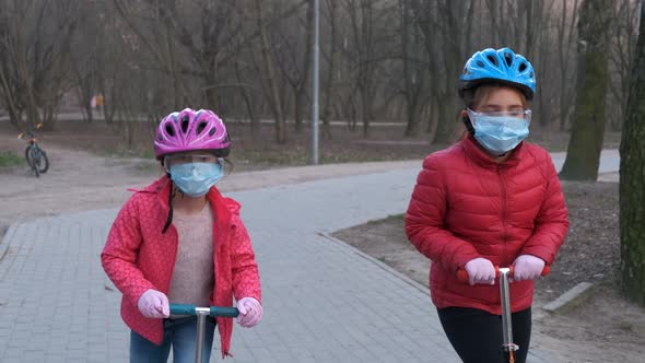 Two little girls, sisters ride scooters in medical masks in the Park.