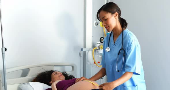 Doctor measuring pregnant womans belly in ward alt