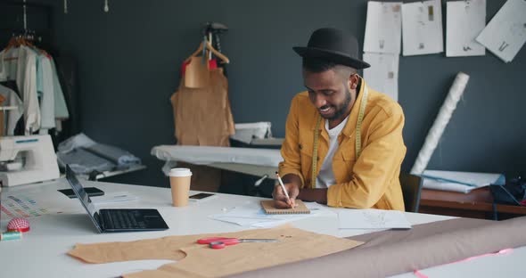 African American Man Designer Writing in Notebook Working in Studio Alone alt