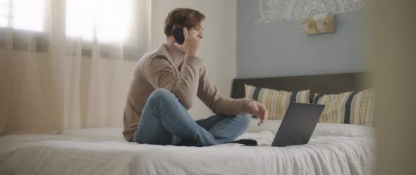 A man answering his phone while working on a computer from home alt