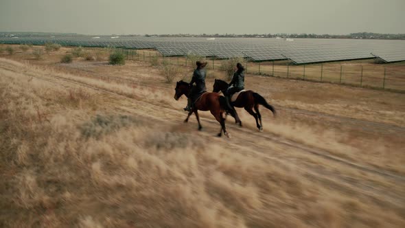 Friends Gallop Riding Horses Along Fields with Solar Panels