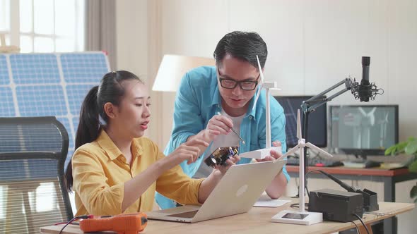 Asian Man And Woman Discuss About Work With Circuit Board, Wind Turbine And Laptop Computer alt