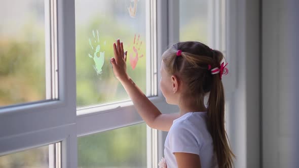 Children girl draw with palms on the window.