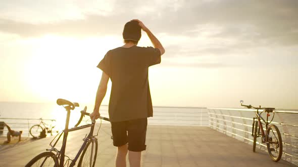 Magnifiecent View From Back of Man with Cap on Backward Coming to the End of Seafront with Bike alt