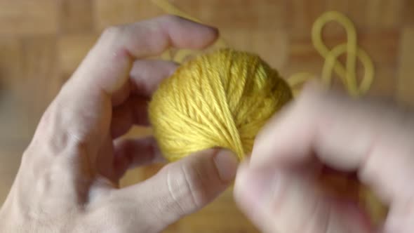 Hand finishing winding ball of yellow wool. Static blur background. Top view alt