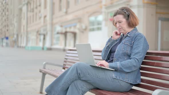 Thinking Old Woman Using Laptop While Sitting Outdoor on Bench alt