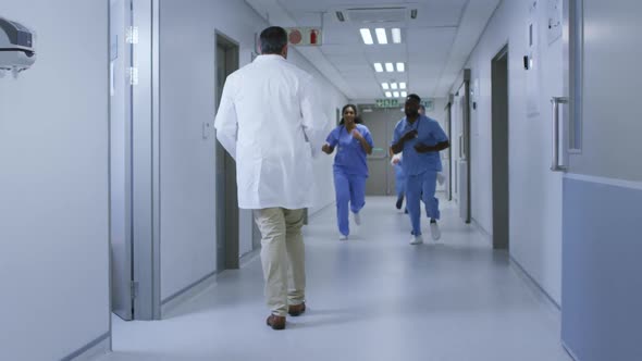 Diverse group of male and female doctors running urgently through hospital corridor alt