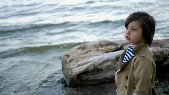 Stylish Boy Child in Red Pants Walking on a Stone Beach alt