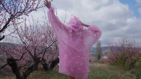 Woman in a Pink Hooded Dress with Flowers Walks Through a Peach Field