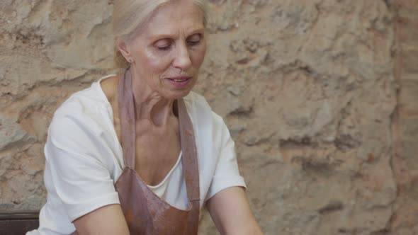 Senior Female Potter Sculpts a Clay Pot alt