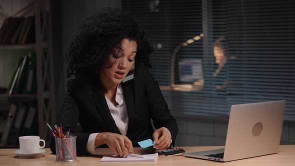 Portrait of African American Woman Talking on Smartphone and Makes Note on Piece of Paper alt
