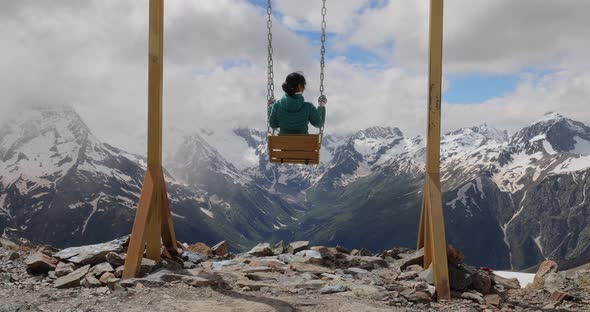 Woman Goes for a Drive on a Swing Against a Background of Mountains alt
