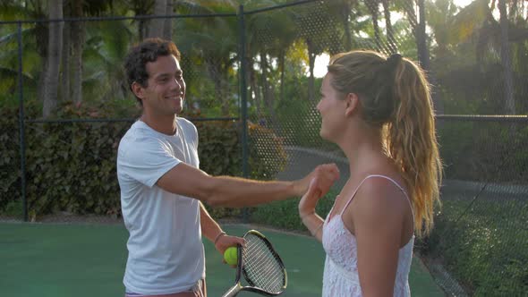 A boyfriend teaching his girlfriend how to play tennis while on vacation. alt