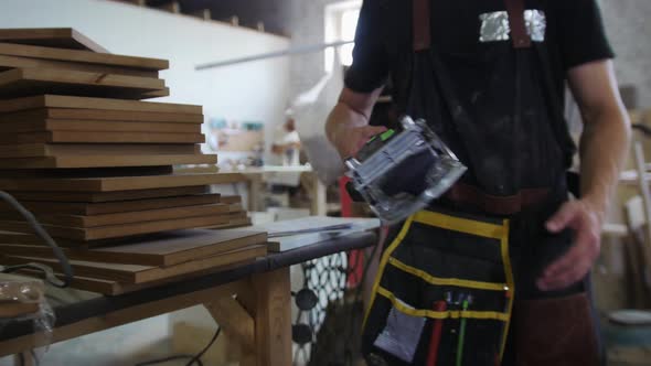 Carpentry Workshop  a Man Worker Walks Along the Studio and Takes the Grinder  Looking in the Camera alt