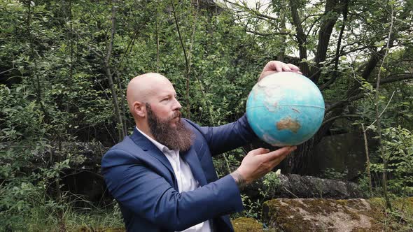 Bearded businessman looking at globe in forest