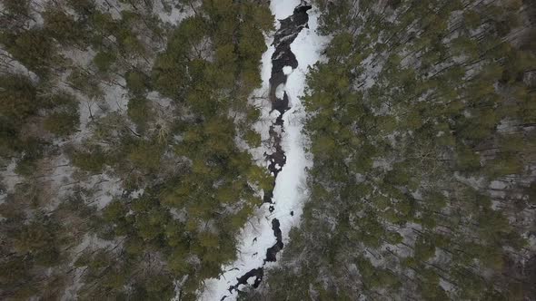 Top down aerial shot of drone going up above snowy river in winter alt