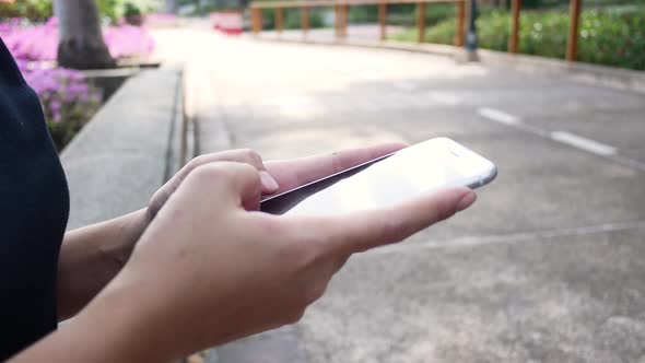 sian young woman sitting at bench in park using smartphone for talking, reading and texting. alt