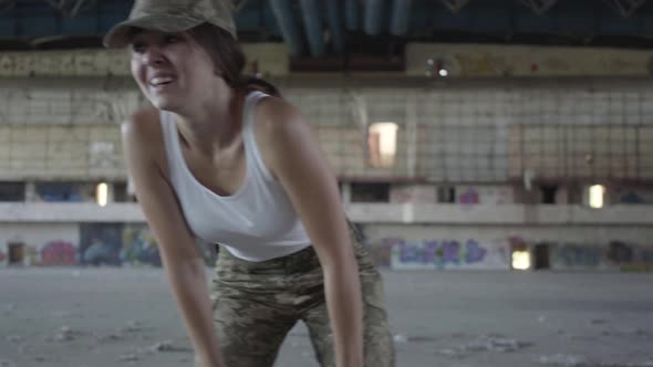 Confident Young Woman in Military Uniform Training in Dusty Dirty Abandoned Building alt