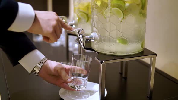 Men's Hands Pour Water Into a Glass From a Glass Decanter with Lemon and Lime