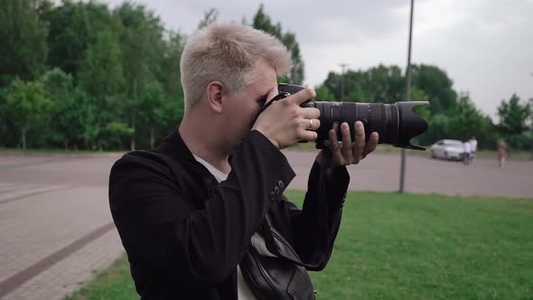 Male photographer takes photos on a professional camera outdoors in park.