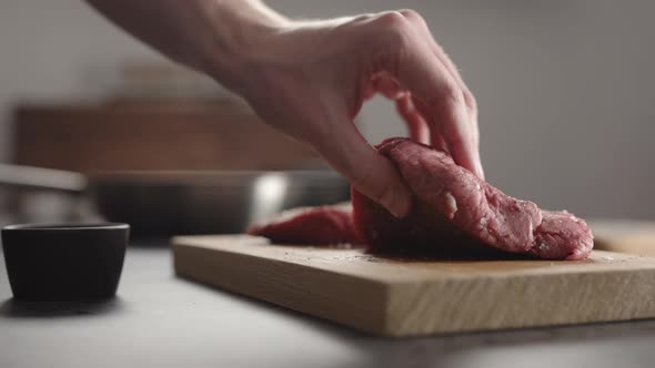 Man Hand Take Seasoned Steak From Wood Board To Put in on a Pan alt
