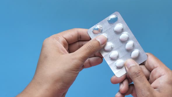  Man Hand Holding Blister Pack Isolated on Blue  alt