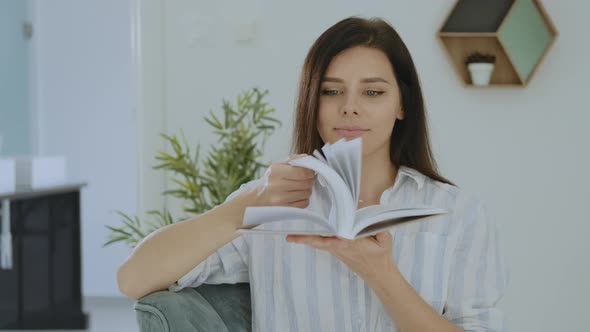 Portrait of pretty young brunette woman smiling and flipping the book at home alt
