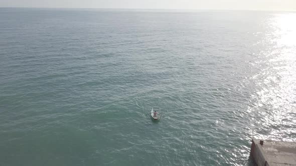 Aerial view of fisherman rowing oars in small fishing boat floating in open sea. Sunlight on water alt