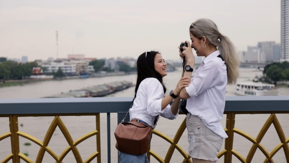 Happy Asian lesbian couple taking a photo while standing on the bridge.