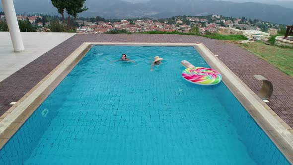 Aerial View of Women Swimming in Pool with Village View