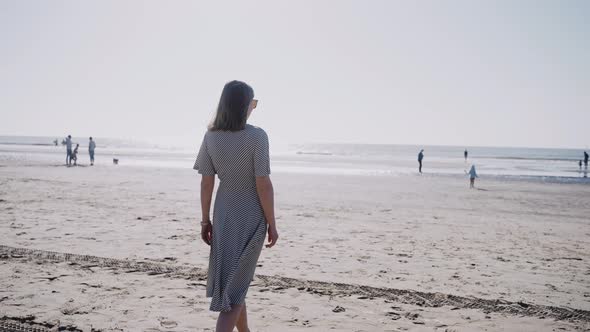 A Woman Walks on an Ocean Beach on a Windy Sunny Day