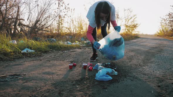 Volunteer Woman Picking Up Trash and Plastics Cleaning the Park with a Garbage Bag. People and alt