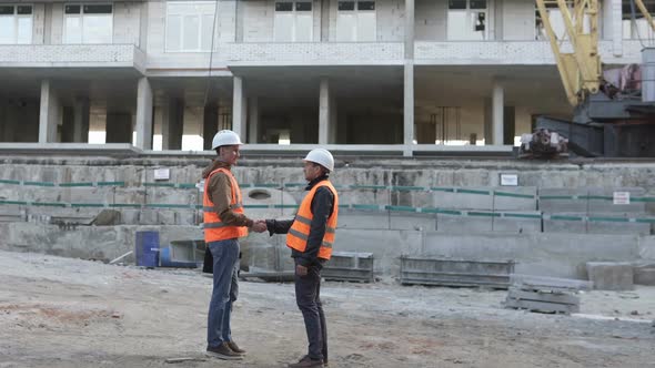 Two construction professionals discussing a construction work plan at a construction site. alt