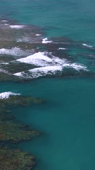 Vertical Aerial Tiltup Shot of Waves Crashing Along Beach with Hills and Clouds