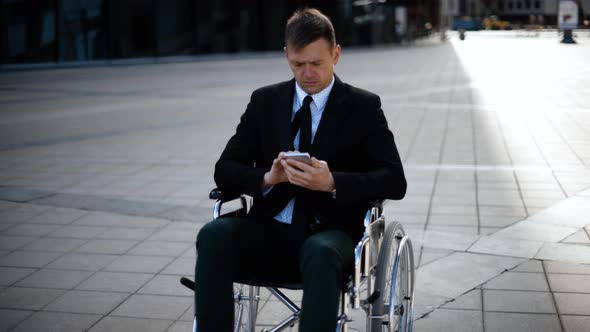 Young Business Man Sitting on Wheelchair Is Playing or Working with His Smartphone alt