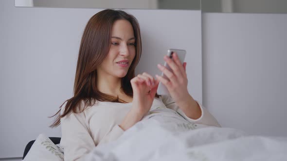 Glad Woman Browsing Mobile Phone on Bed alt