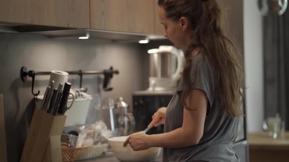 A young woman is at home in the kitchen preparing food alt