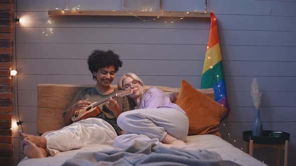 A Young LGBT Couple Lies in Bed in the Evening and Plays the Ukulele