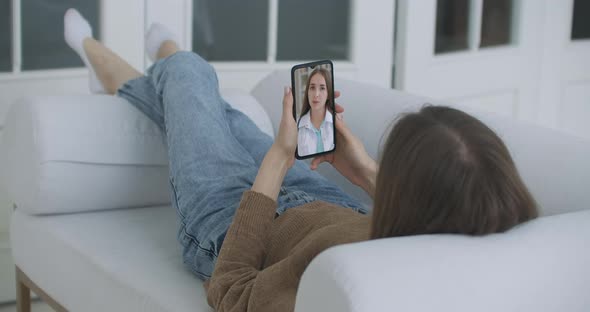 Young Female Sick at Home Using Smartphone To Talk To Her Doctor Via Video Conference Medical App alt