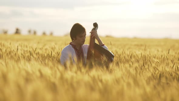 Young Man Playing on Bandura in Beautiful Wheat Field