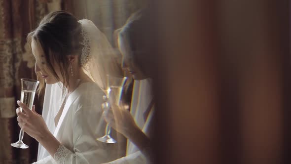 Beautiful and Lovely Bride in Night Gown and Veil Sitting and Drinking Champagne alt