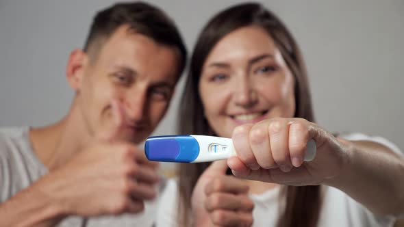 Closeup of Positive Pregnancy Test on Blurred Background of Happy Man and Woman Slow Motion alt
