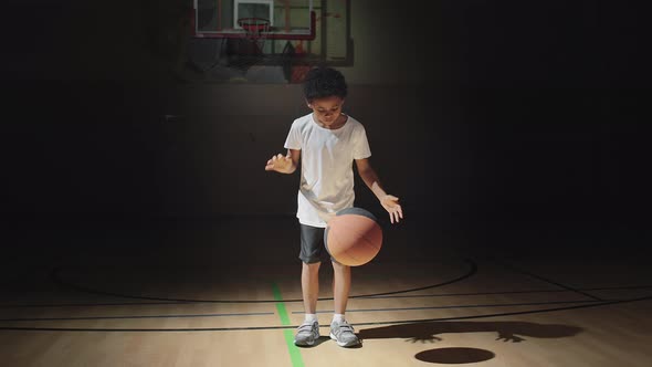 Cute Boy Dribbling Ball on Dark Basketball Court alt
