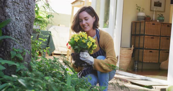 Smiling caucasian woman planting yellow flowers in sunny garden her pet dog watching her alt