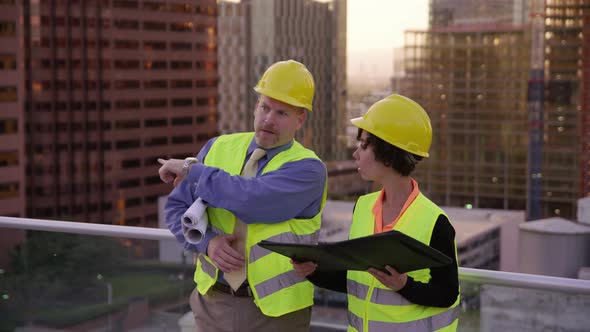 Two construction supervisors look at plans on rooftop