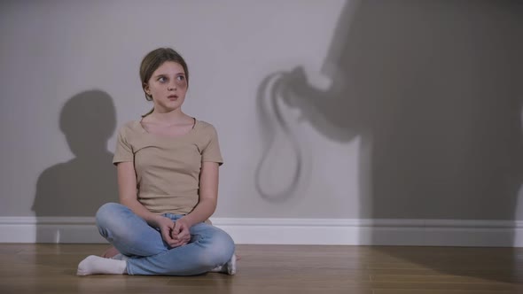 Scared Girl Looking Away Hugging Self As Parent Shadow Frightening Teenager with Belt alt