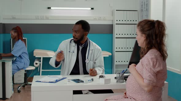 Male Obstetrician Giving Bottle of Pills to Woman with Baby Bump alt