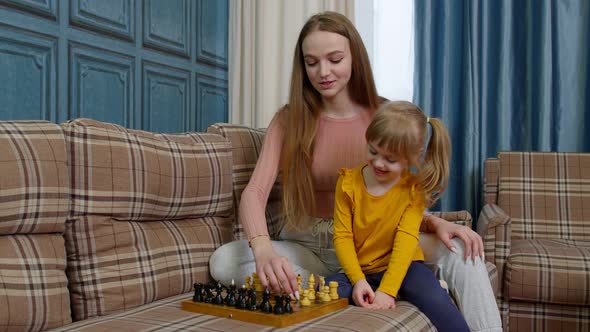 Happy Young Mother Woman Teaching Small Child Daughter Playing Chess on Wooden Board at Home Sofa alt