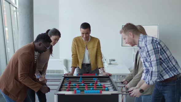 Young handsome casual multiethnic business people playing table football and relaxing at office