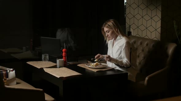 a Lonely Woman Sits on a Sofa in a Restaurant Cutting Food and Eating